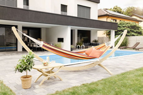 Colourful hammock on a stand by a poolside patio with a modern house in the background
