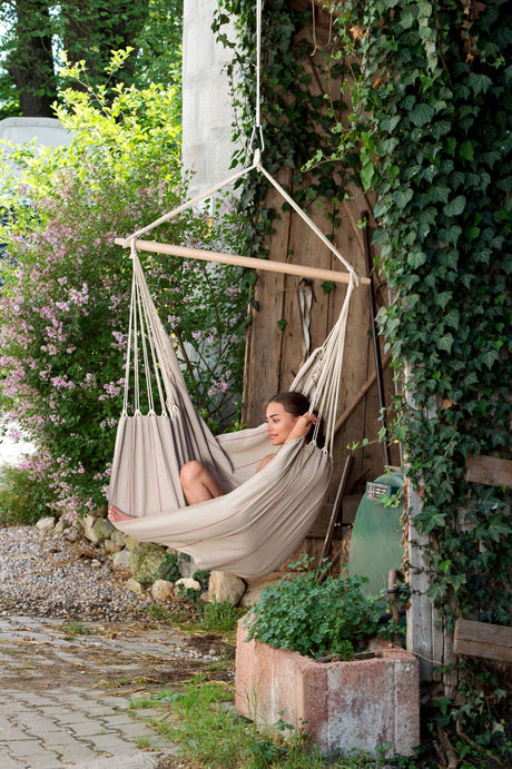 Woman relaxing in a beige hammock surrounded by greenery and a rustic wooden door.