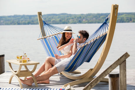 Two people relaxing in a blue and white striped hammock by a lake.
