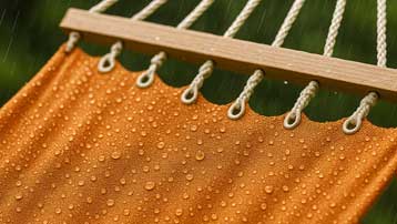 Orange hammock with water droplets on a wooden frame against a blurred green background