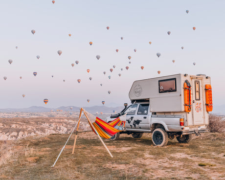 Camper van with a hammock in a field with hot air balloons in the sky
