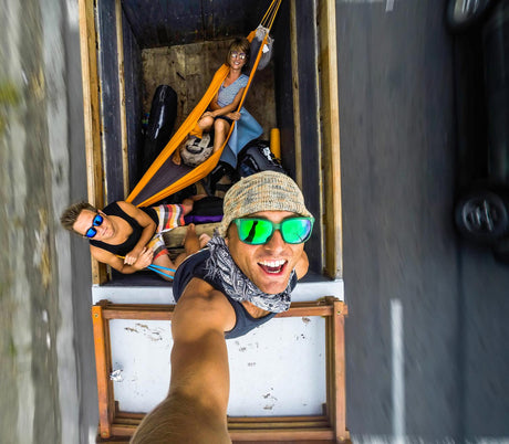 Two people are on a hammock inside a wooden structure, with a third person sitting above them.