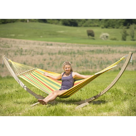 Woman relaxing in a colourful striped hammock in a grassy field.