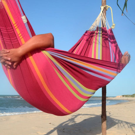 Person relaxing in a colourful striped hammock on a beach.