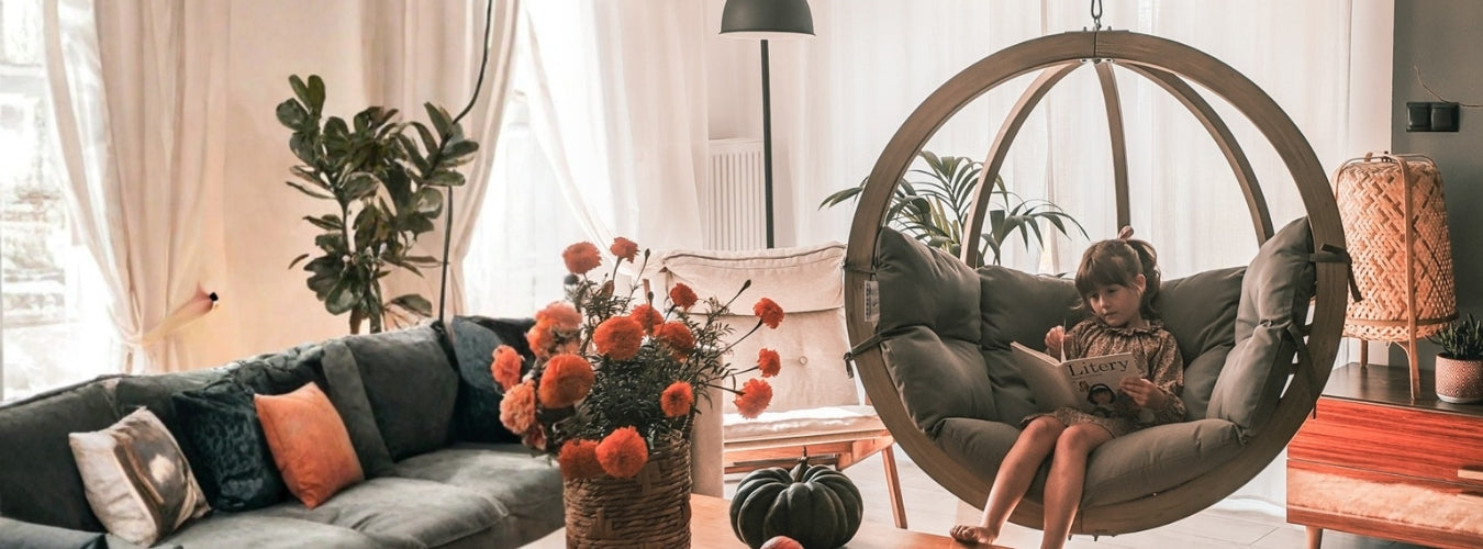 A woman sitting in a hanging chair in a cosy living room with a vase of flowers and a couch.