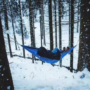 Person lying in a blue hammock in a snowy forest