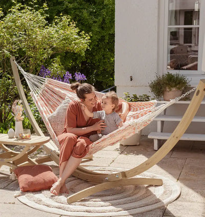 Woman and child in a non spreader bar hammock on a patio with a garden background