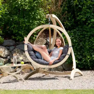 Person relaxing in a hanging wooden egg chair in a garden setting