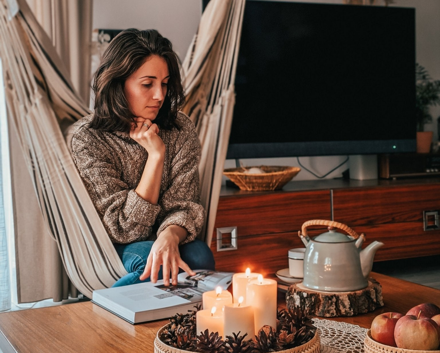 Woman reading a book in a hammock with candles and a teapot on a table.