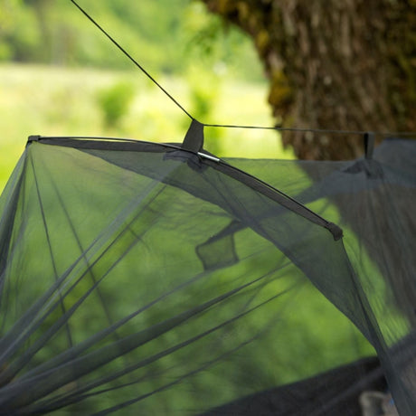 A close-up of a mosquito net spreader bar, set against a blurred outdoor background with a tree trunk and green grass.
