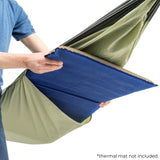 A person is holding up a blue thermal mat insert inside an olive green camping hammock. The image is shot against a clean white background with a small text note in the bottom right corner that says '*thermal mat not included'.