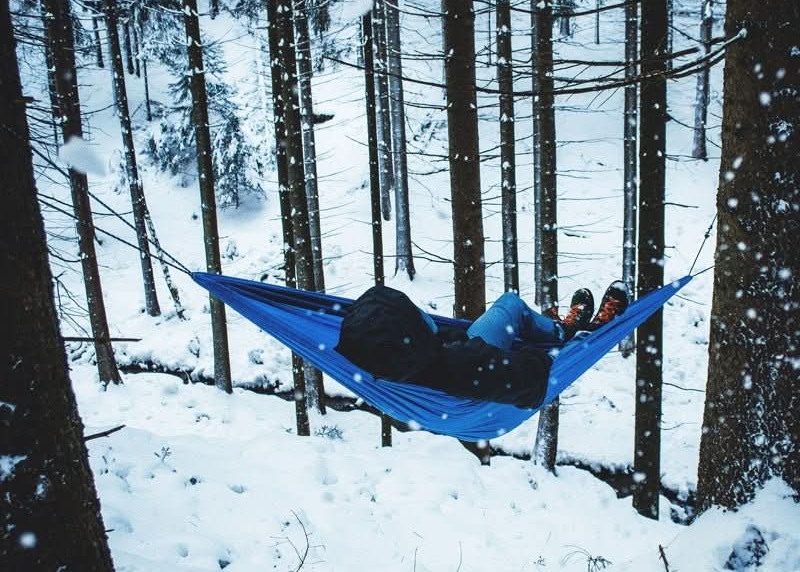 Person in a blue hammock in a snowy forest