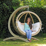 A woman sitting in a wooden hanging chair with a white cushion in a garden setting.
