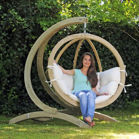 A woman sitting in a wooden hanging chair with a white cushion in a garden setting.