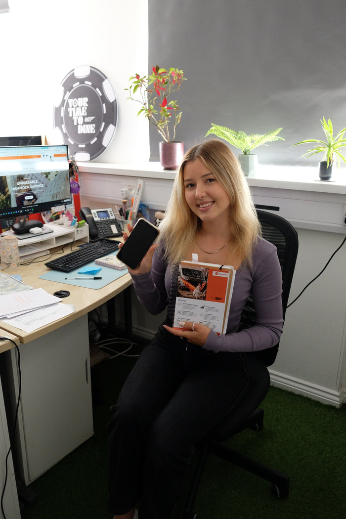 A woman sitting at a desk holding a book, with office equipment and plants in the background.