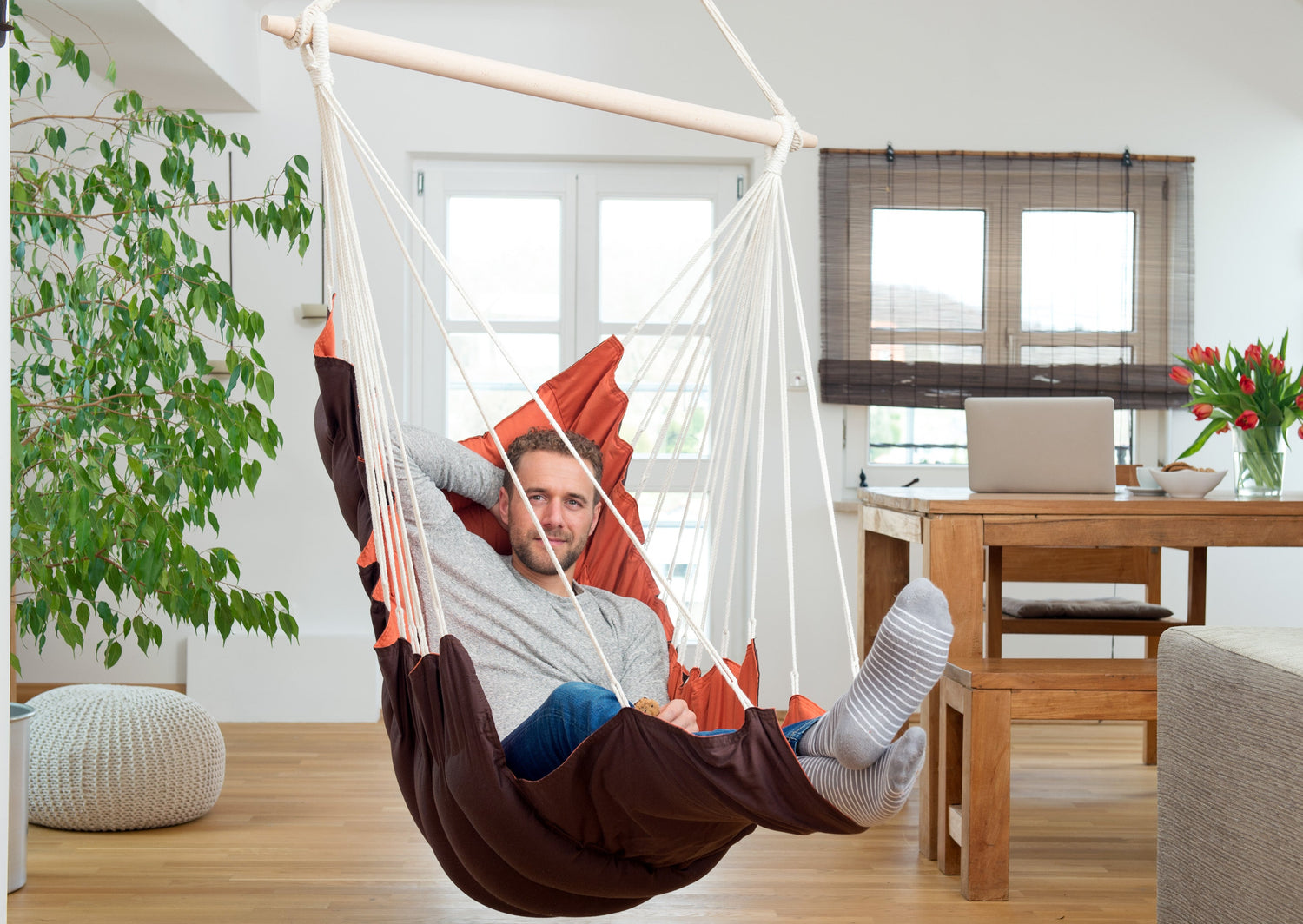 A man is relaxing in a brown hammock chair in a modern living room.