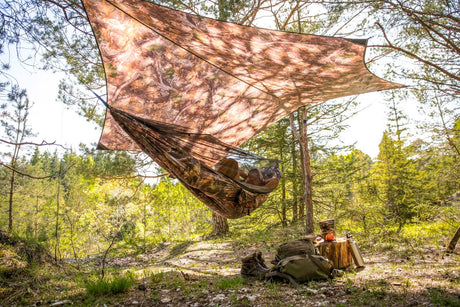 A camouflage hammock hanging between trees in a forest setting