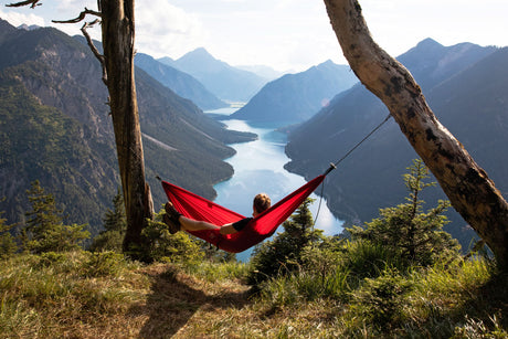 Person in a red hammock overlooking a mountain lake with a scenic view.