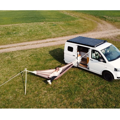 Person relaxing in a hammock outside a white camper van in a grassy field.