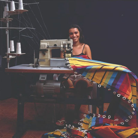 A woman sitting at a sewing machine with colourful fabric in a dark room