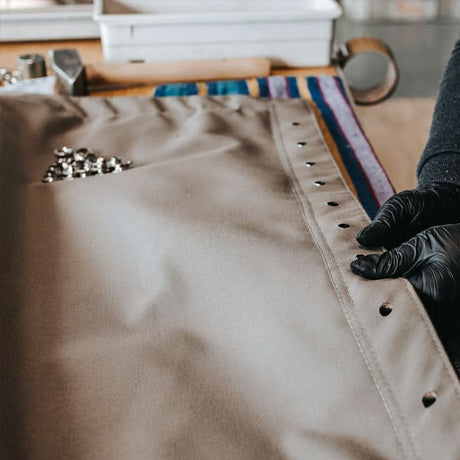 Person wearing black gloves working on a leather product with tools in the background