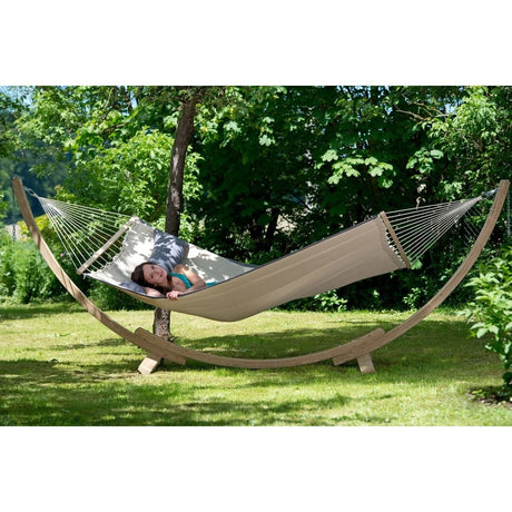 Person lying in a beige hammock with a wooden stand in a garden setting.