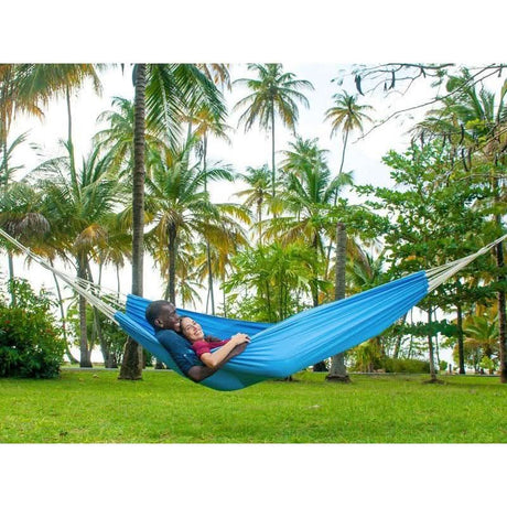 Two people in a blue hammock surrounded by palm trees