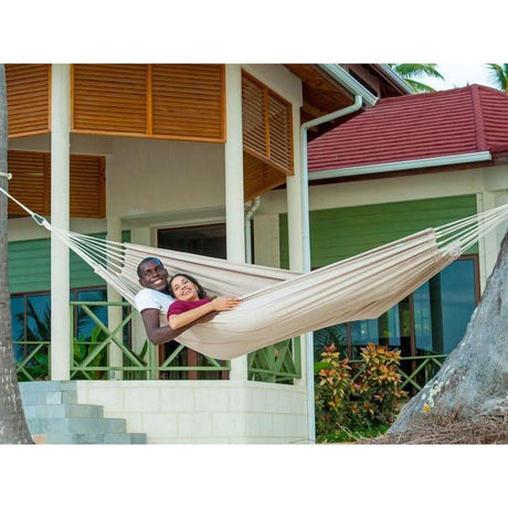 Two people in a beige hammock in front of a colourful house.