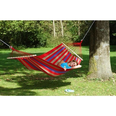 Person relaxing in a red, blue, and white striped hammock in a park.