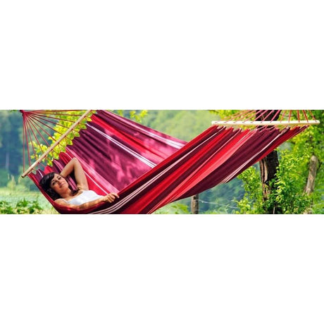 Person relaxing in a red hammock with a green forest background