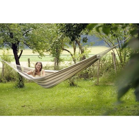 A woman relaxing in a hammock in a natural setting with trees and grass.