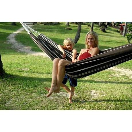 Woman and child in a striped hammock on a grassy area with trees in the background