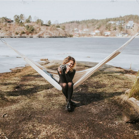 Person sitting in a hammock by a lake with a scenic background