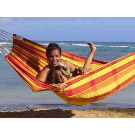 Two people in a colourful hammock on a beach with the ocean in the background