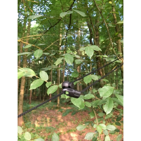 Close-up of a black hammock clip attached to tree branches with a forest background