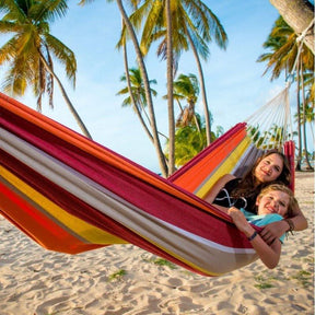 Two people in a colourful striped hammock on a beach with palm trees in the background