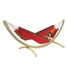 Red and orange striped hammock on a wooden stand with a person sitting inside.