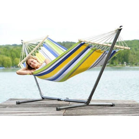Colourful striped hammock on a stand with a person relaxing, set against a scenic lake backdrop.