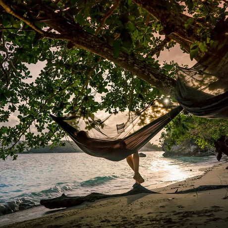 Person relaxing in a hammock on a beach with an ocean view