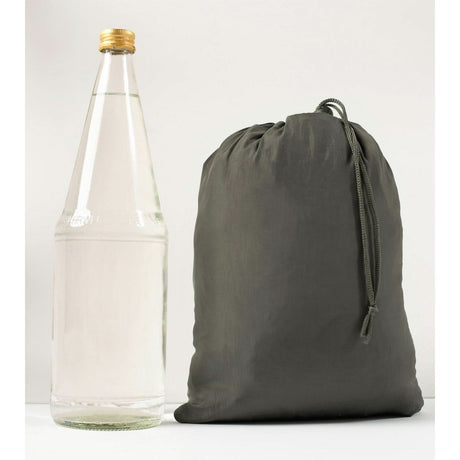 Clear glass bottle with gold cap next to a grey drawstring bag on a white background