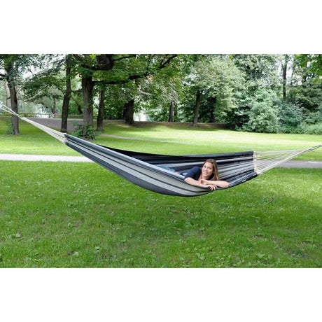 Person lying in a hammock on a grassy area with trees in the background
