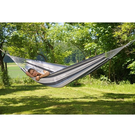 Person relaxing in a striped hammock surrounded by trees and greenery