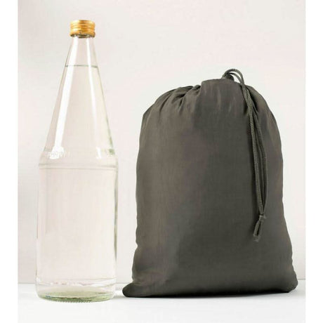 Grey drawstring bag next to a clear glass bottle with a gold cap on a white background