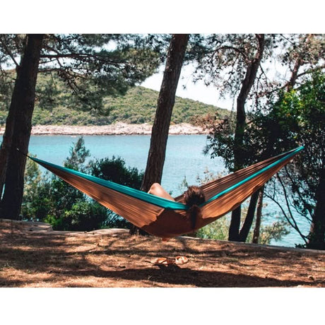 Person relaxing in a hammock by a lakeside surrounded by trees