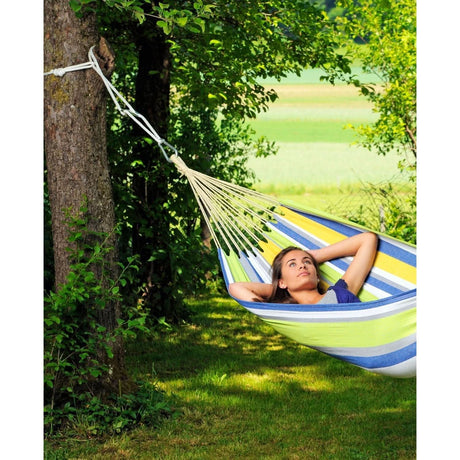 Person relaxing in a striped hammock under a tree in a park