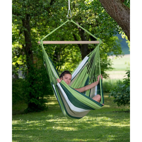 Person relaxing in a green and white hammock swing surrounded by trees.