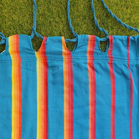 Close-up of a colourful striped hammock with blue straps on grass.
