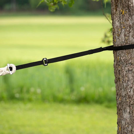 Black strap attached to a tree with a blurred green field background