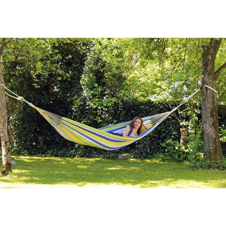 Person relaxing in a colourful striped hammock surrounded by greenery