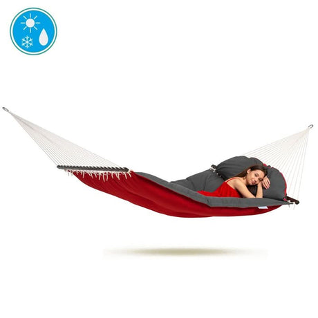 Person lying in a red and grey hammock with a backpack on a white background